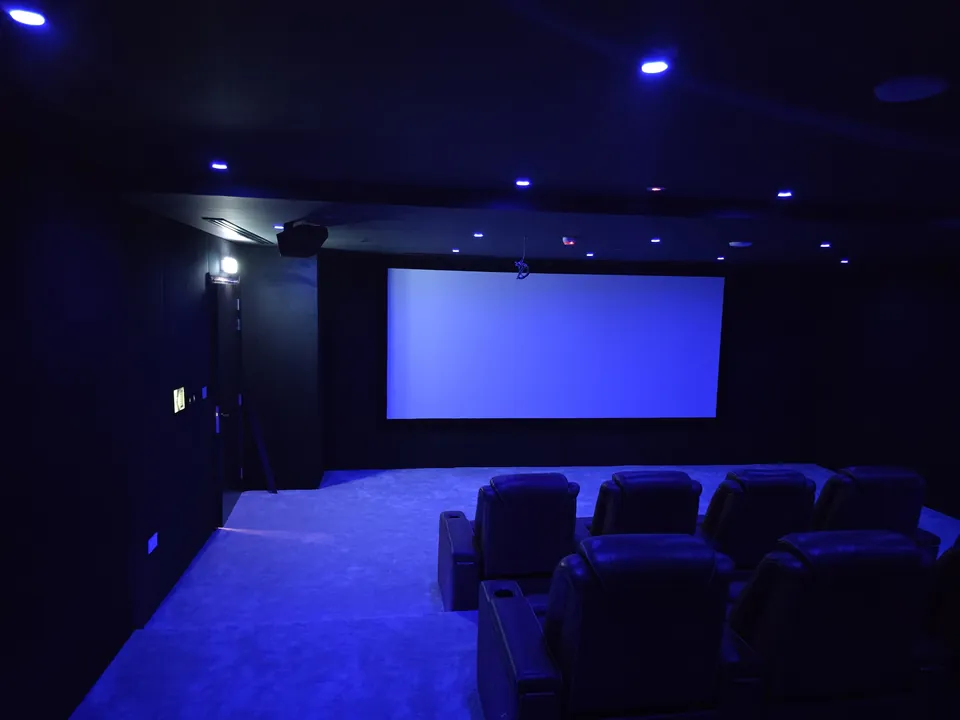 The finished room in blue ambient light, rows of seats facing the wide screen