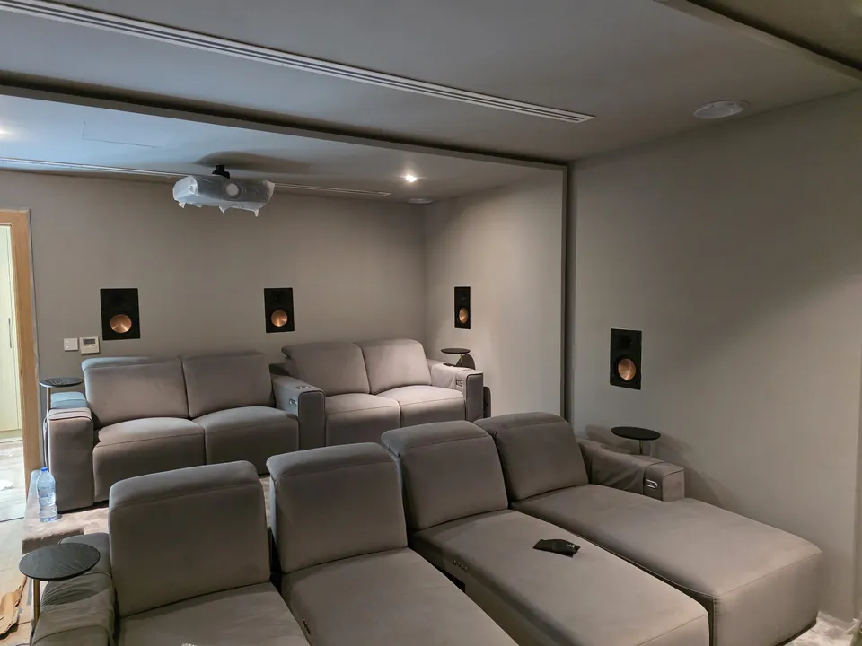 Two rows of grey fabric recliners facing the screen wall, with in-wall speakers on the side walls