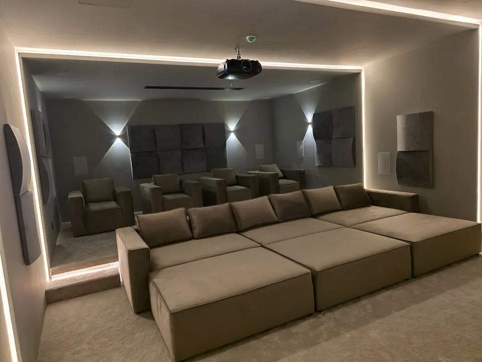 A cinema room framed by LED light lines, with two rows of lounge seating facing the screen